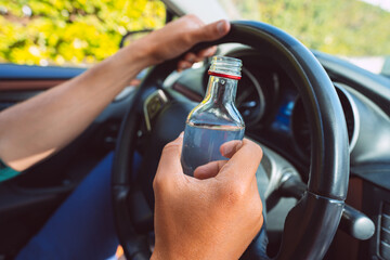 Closeup of drunk man hands on the steering wheel with a bottle of vodka. Driving under alcohol influence
