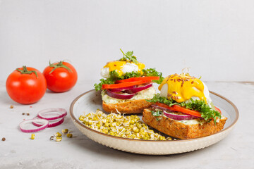 Sandwiches with poached egg on a vegetable bun, with soft cheese, fresh vegetables, with mustard sauce. On a plate of mung bean sprouts. Close-up on a light background.