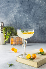 Gin and tonic cocktail with kumquat fortunella in glass of champagne on light gray table surface.