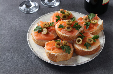 Canapes of salted salmon, green olives and parsley on croutons of white bread on dark gray background. Festive snack. Closeup