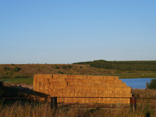 Summer countryside landscape. A large haystack for animals and in the distance a pond for growing...