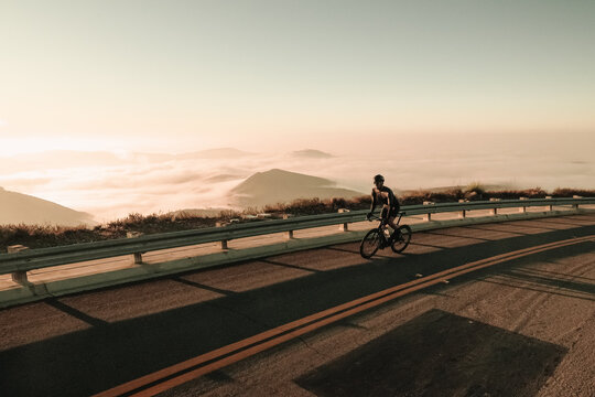 A Road Bike Cyclist Climbs A Hill Pedaling Up A Steep Road During A California Sunrise Above The Clouds.