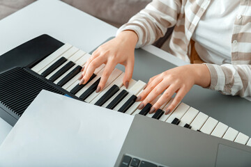 Fototapeta na wymiar Woman playing piano record music on synthesizer using notes and laptop. Female hands musician pianist improves skills playing piano. Online Music education hobby vocals singing using piano.