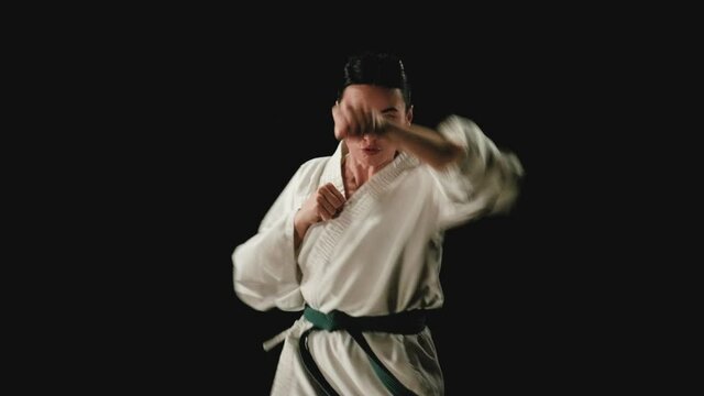 Young woman in kimono practicing karate kicks on a black background. Slow motion