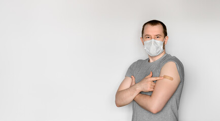 A young adult man wearing a protective face mask shows his arm after vaccination. Theme immunization during pandemic covid-19. Space for text, selective focus