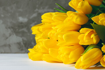 Bouquet of bright yellow tulips lying on white wooden surface on gray background. Copy space