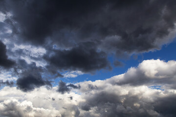 Obraz premium Thunderstorm clouds texture. Epic storm sky with dark grey and white cumulus clouds against blue sky background