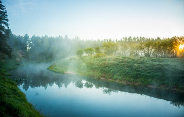 Fototapeta na wymiar A beautiful spring landscape of a river valley with morning mist. Springtime scenery of a river flowing through the forest. Water evaporating in sun rays. Springtime scenery of Northern Europe.