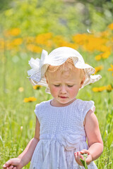 Portrait of beautiful little girl on background of yellow flowers in a meadow. happy childhood in nature. Walking while quarantine away from people
