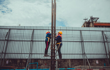 Two female laborers are tying the steel bar to the concrete pole.