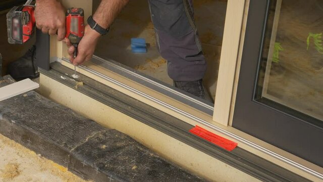 CLOSE UP: Unrecognizable contractor drills a hole while mounting a window at a housing project under construction. Carpenter bores uses a power drill to bore a hole as he installs a sliding door.