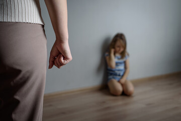 An angry mother stands in a threatening pose over a little girl sitting on the floor. Domestic...
