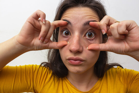 Woman in yellow t-shirt on white background bugging her eyes