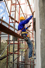 A plasterer stands on a scaffold to plaster the outside of the building.