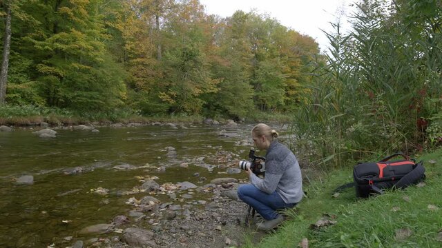 Young male filmmaker shoots footage by a stream near a forest, camera operator