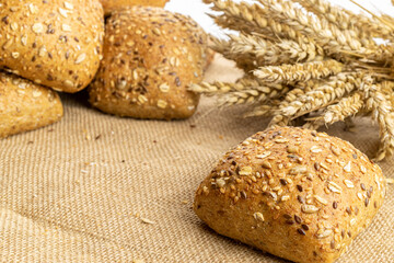 Rustic bread. Fresh loaf of rustic traditional bread with wheat grain ear or spike plant on linen texture background. Rye bakery with crusty loaves and crumbs. Concept - Cooking at Home.