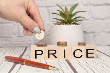 The concept of price, money, finance or savings by using a cubic wooden block with letters, the hand folds the coins on a light wooden table