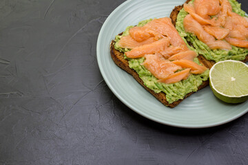 Tasty sandwich with dark rye bread, avocado and salmon. Homemade toast on gray concrete background. Gray background, top view, free space. Healthy protein food, breakfast, lunch concept. Gourmet snack