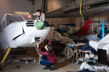 Adult male aircraft enthusiast with female assistant working in workshop on creating of light aircraft flying model
