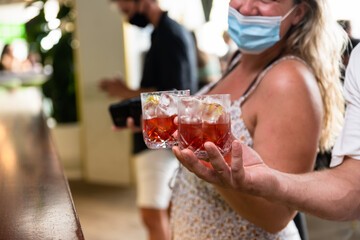 Mask wearing Patrons hold cocktails in a Bar setting 