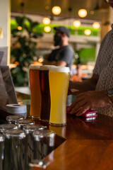 Three shades of Craft Beer in Tall glasses upon a bar, bearded man in background