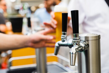 Silver Beer taps with black handles covered in condensation with a hand serving a tall glass of amber coloured beer in the background with a perfect head 