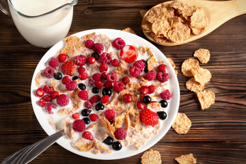 A bowl of cereal and berries with milk on a wooden table. Healthy summer breakfast