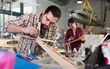 Fototapeta na wymiar Young man hobbyist engaged in modeling plane models in aircraft workshop