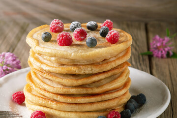 Stack of pancakes with fresh berries on a white plate on the table