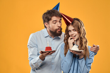 Man and woman at a party in caps and with tinsel cake fun yellow background