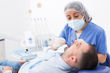 Professional dentist woman inspects patient teeth with dental tools - mirror and probe