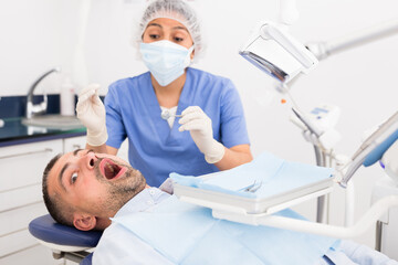 Professional dentist woman inspects patient teeth with dental tools - mirror and probe