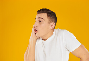Emotional guy in a white T-shirt on a yellow background gestures with his hands to the surprise model