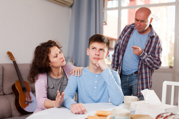 Offended teenager sitting at home, listening to reprimanding from his parents ..