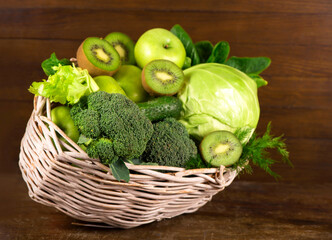 Green vegetables - kiwi, cabbage, herbs, celery, broccoli, cucumbers in a basket a wooden background
