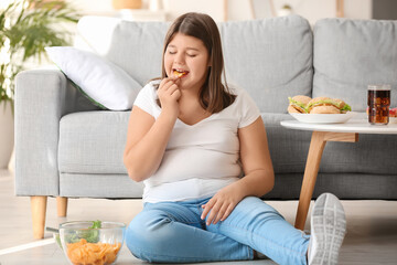 Obraz na płótnie Canvas Overweight girl eating unhealthy chips at home