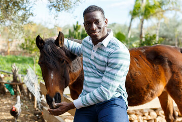 African American male farm owner posing with horse at sunny day