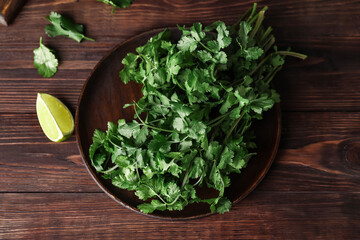 Plate with fresh cilantro and lime on wooden background