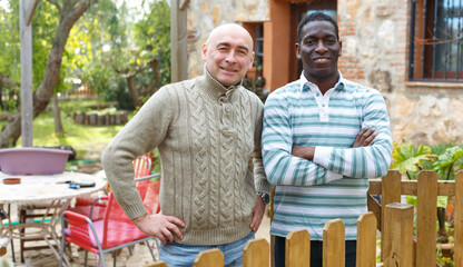 Portrait of two friendly male farmers standing near wooden fence on courtyard of farmhouse..