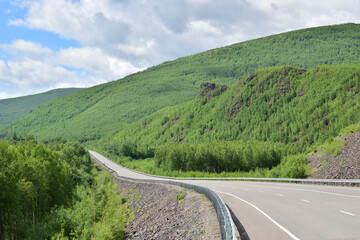 An asphalt road among the green hills. A bright summer day. Sikhote-Alin Mountains.