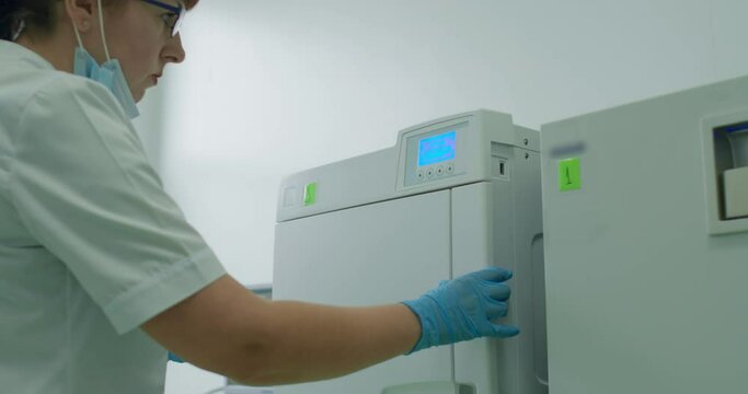 A female medical worker is close the door of the dental sterilizer and turn on the timer for sterilization of the dental tools.