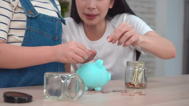 Asian Mother Is Teaching Her Daughter About Money Saving And Financial Planning By Using Piggy Bank