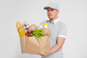 portrait of delivery man in uniform giving the paper bag full of products over white