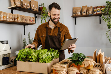 Smiling bearded seller man using tablet computer in local eco shop