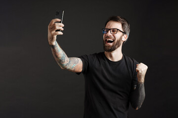 Excited man taking selfie on cellphone and making winner gesture