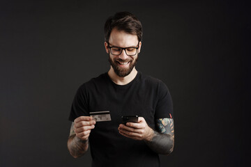 Bearded happy man smiling while using cellphone and credit card