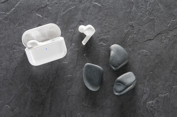 White wireless headphones with charging box on a concrete background, decorated with stones.