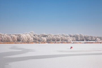 Winterlandschaft eines Sees bedeckt mit Eis und Schnee unter blauem, wolkenlosem Himmel