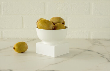 kiwi in a white bowl on a podium om a marble kitchen table. Fresh juicy tropical fruits
