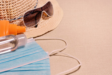 Beach hat, sunglasses, face medical mask, sunscreen and sanitizer on the beach background. Travel, vacation,Coronavirus,Covid-19,pandemic, quarantine,safe vacation. Flat lay.Top view.Copy space.